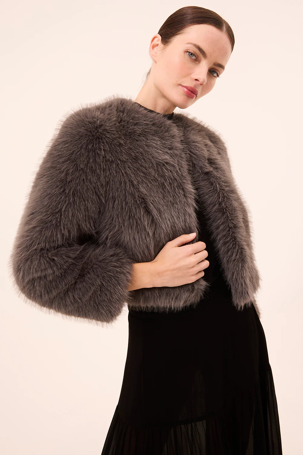 Woman wearing a gray fur shrug over a black dress against a beige background