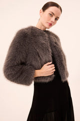 Woman wearing a gray fur shrug over a black dress against a beige background